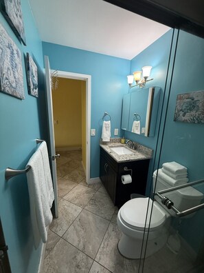 A bathroom with a blue wall, a white toilet, a sink with a mirror, and a towel rack. - Island Couples Retreat - 1 Bed Condo in Red Hook (Red Hook)