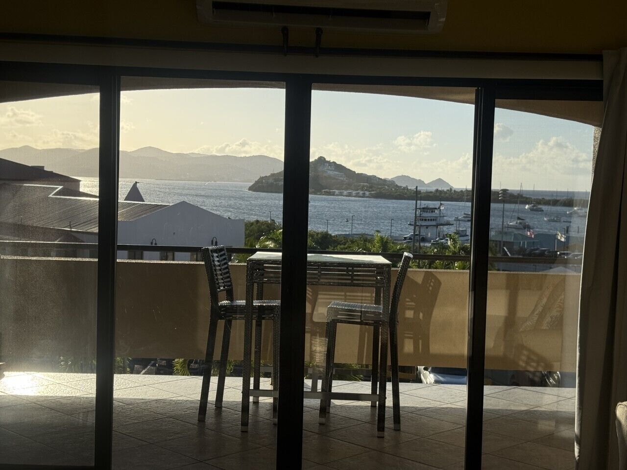 Een balkon met een tafel en stoelen, met uitzicht op een jachthaven met boten en heuvels in de verte.
