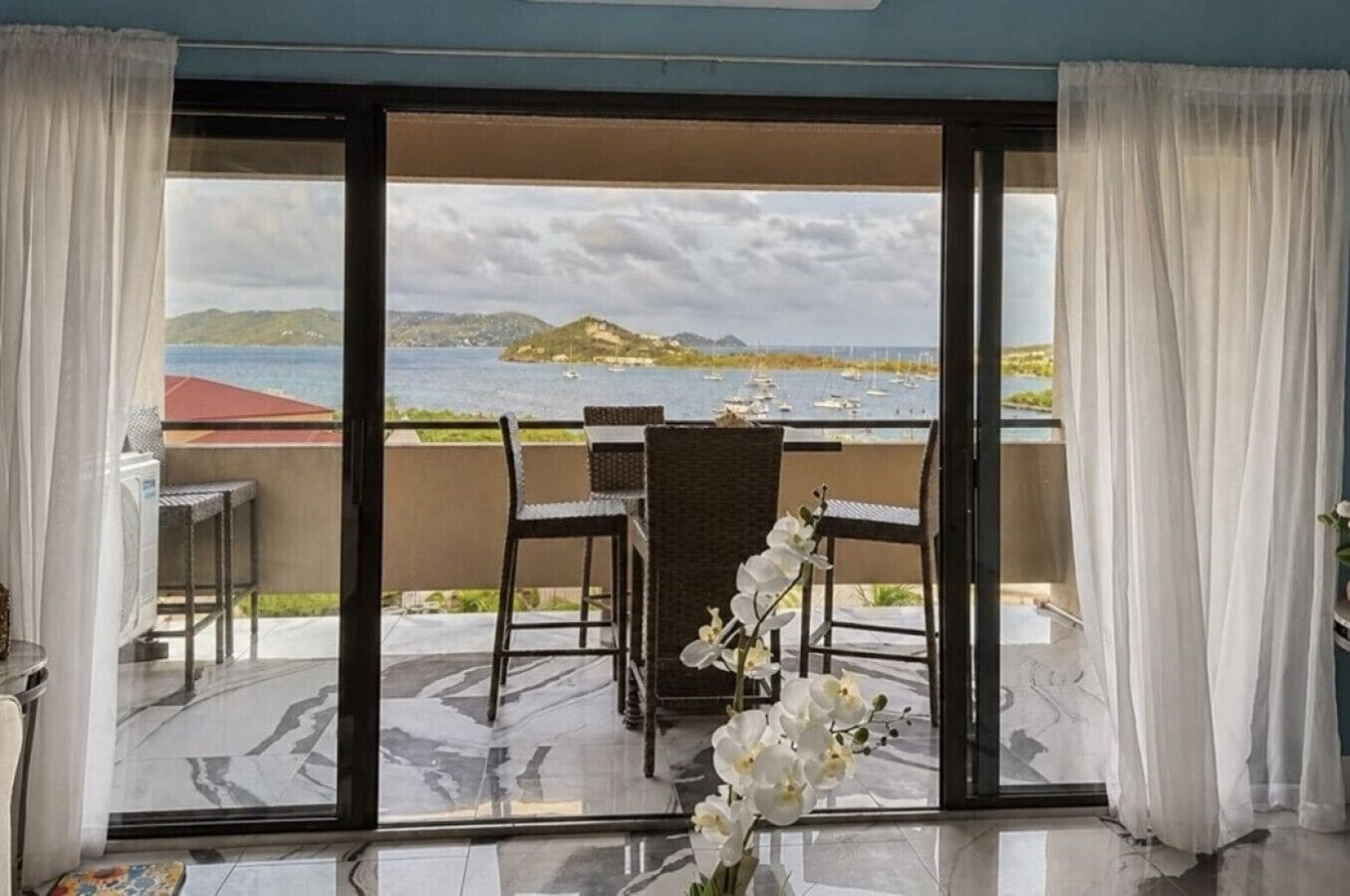 A balcony with a table and chairs, a view of the sea, and a mountainous landscape.