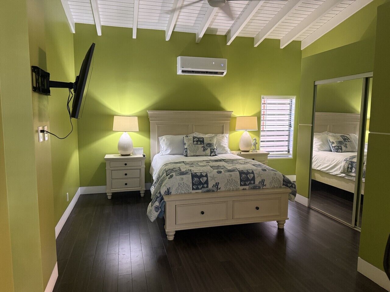 A bedroom with a bed, nightstands, a mirror, and an air conditioning unit.