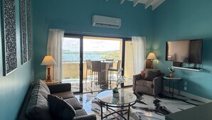 Ein Wohnzimmer mit Sofa, Couchtisch und Fernseher. Ein Balkon bietet Blick auf das Meer.