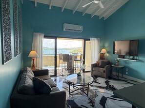 A living room with a sofa, a coffee table, and a TV. There is a balcony with a view of the sea. - Spacious 2BR Retreat • Balcony Views + Parking (Red Hook)