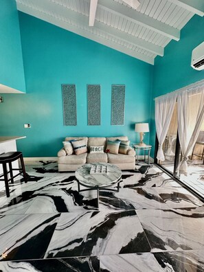 A teal-walled room with a sofa, a coffee table, and a patterned floor. - Spacious 2BR Retreat • Balcony Views + Parking (Red Hook)