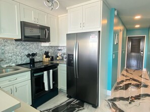 A modern kitchen with white cabinets, a stainless steel refrigerator, a microwave, and a granite countertop. - Spacious 2BR Retreat • Balcony Views + Parking (Red Hook)