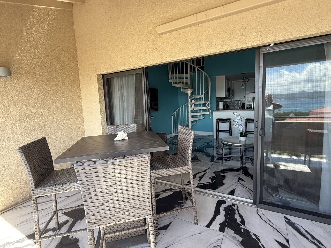 A balcony with a dining table and chairs, a staircase, and a view of the sky.