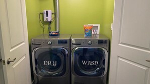 Ein Waschraum mit zwei Waschmaschinen, die nach 'DRY' und 'WASH' beschriftet sind, einem Warmwasserbereiter und einer Tide Waschmittelkarton.