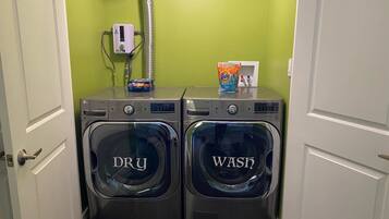 A laundry area with two front-loading washing machines labeled 'DRY' and 'WASH,' a water heater, and a Tide detergent box.