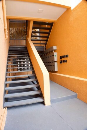A staircase with metal railings, a yellow wall, and electrical boxes on the right. - Spacious 2BR Retreat • Balcony Views + Parking (Red Hook)