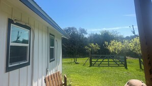 Ein Haus mit einer Veranda, einem Holzstuhl, einem Tor und einem grünen Rasen.