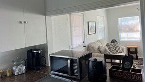 Eine Küche mit Mikrowelle, Kaffeemaschine und einem Kaffeeautomaten. Im Hintergrund befinden sich ein Sofa und ein kleiner Tisch.