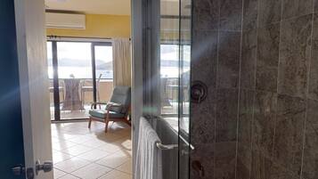 A bathroom with a glass shower door, a towel hanging on the door, and a view of an outdoor balcony with a chair and table.