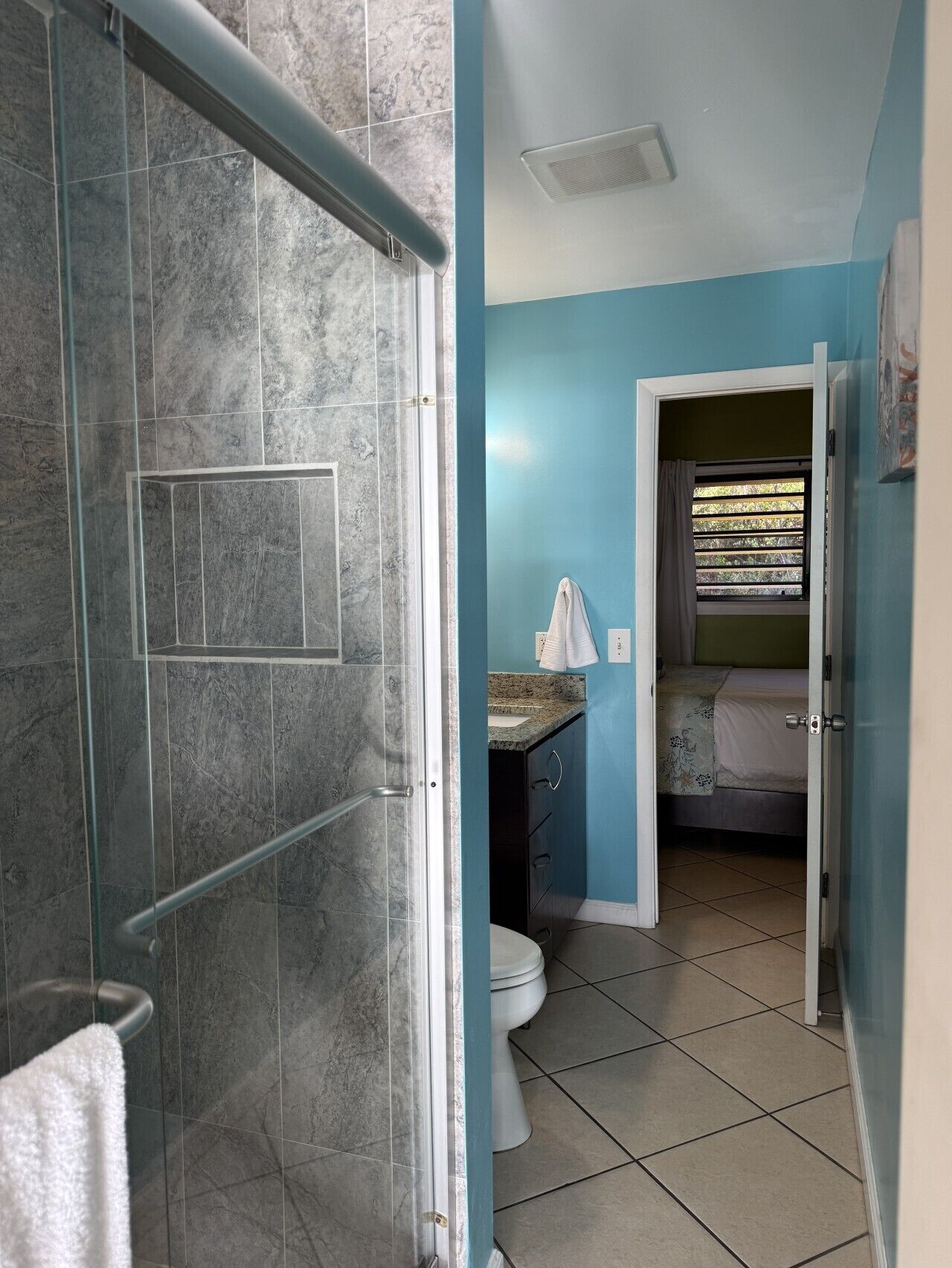 Une salle de bain avec une douche à parois de verre, des toilettes et un lavabo, avec une serviette accrochée au mur.