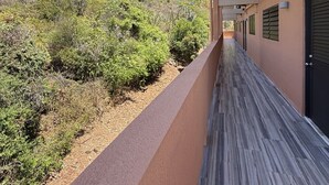 A corridor with a view of a hillside, a building with a beige facade, and a clear sky. - Walk to Ferry • Red Hook 1BR Condo w/ Stunning Balcony Views + Free Parking (Red Hook)