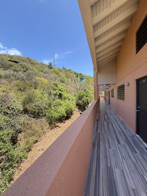 A corridor with a view of a hillside, a building with a beige facade, and a clear sky. - Walk to Ferry • Red Hook 1BR Condo w/ Stunning Balcony Views + Free Parking (Red Hook)