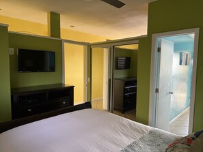 A bedroom with a bed, a TV, a dresser, and a door leading to another room. - Walk to Ferry • Red Hook 1BR Condo w/ Stunning Balcony Views + Free Parking (Red Hook)