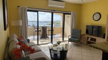 A living room with a sofa, a coffee table, a TV, and a balcony with a view of the sea.