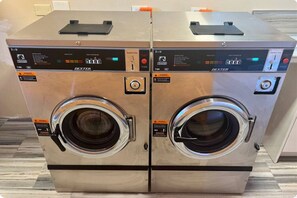 Two Dexter brand front-loading washing machines in a commercial setting. - Walk to Ferry • Red Hook 1BR Condo w/ Stunning Balcony Views + Free Parking (Red Hook)