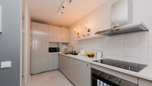 A modern kitchen with white cabinets, a built-in oven, and a stainless steel range hood. - Shortstaypoland Mokotowska (Warsaw)