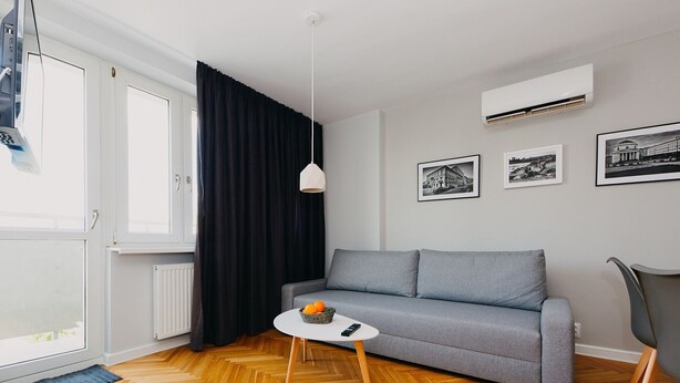 A modern living room with a grey sofa, a small round table with a basket, and a black chair. - Shortstaypoland Mokotowska (Warsaw)