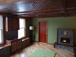 Una habitación con vigas de madera, chimenea, pared verde y ventana.