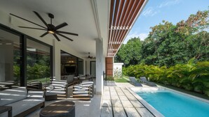 Ein moderner Poolbereich im Freien mit Sitzgelegenheiten, Deckenventilatoren und üppiger Bepflanzung.