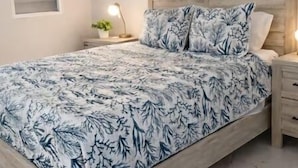 Ein Schlafzimmer mit einem Bett, einem Deckenventilator, zwei gerahmten Bildern, einem Nachttisch und einer Nachttischlampe.