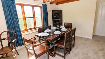 A dining room with a wooden table set for four, flanked by two chairs, a cabinet with dishes, and a window with curtains.