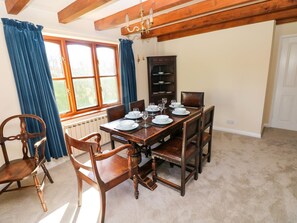 Una sala da pranzo con un tavolo di legno apparecchiato per quattro persone, affiancato da due sedie, un mobile contenitore con stoviglie e una finestra con tende.