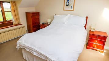 A bedroom with a bed, a dresser, a nightstand, a radiator, and a window with curtains.
