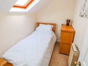 A small, single-bed room with a skylight, a wooden bedside table, and a radiator. - Park Hall Cottage (Haverfordwest)