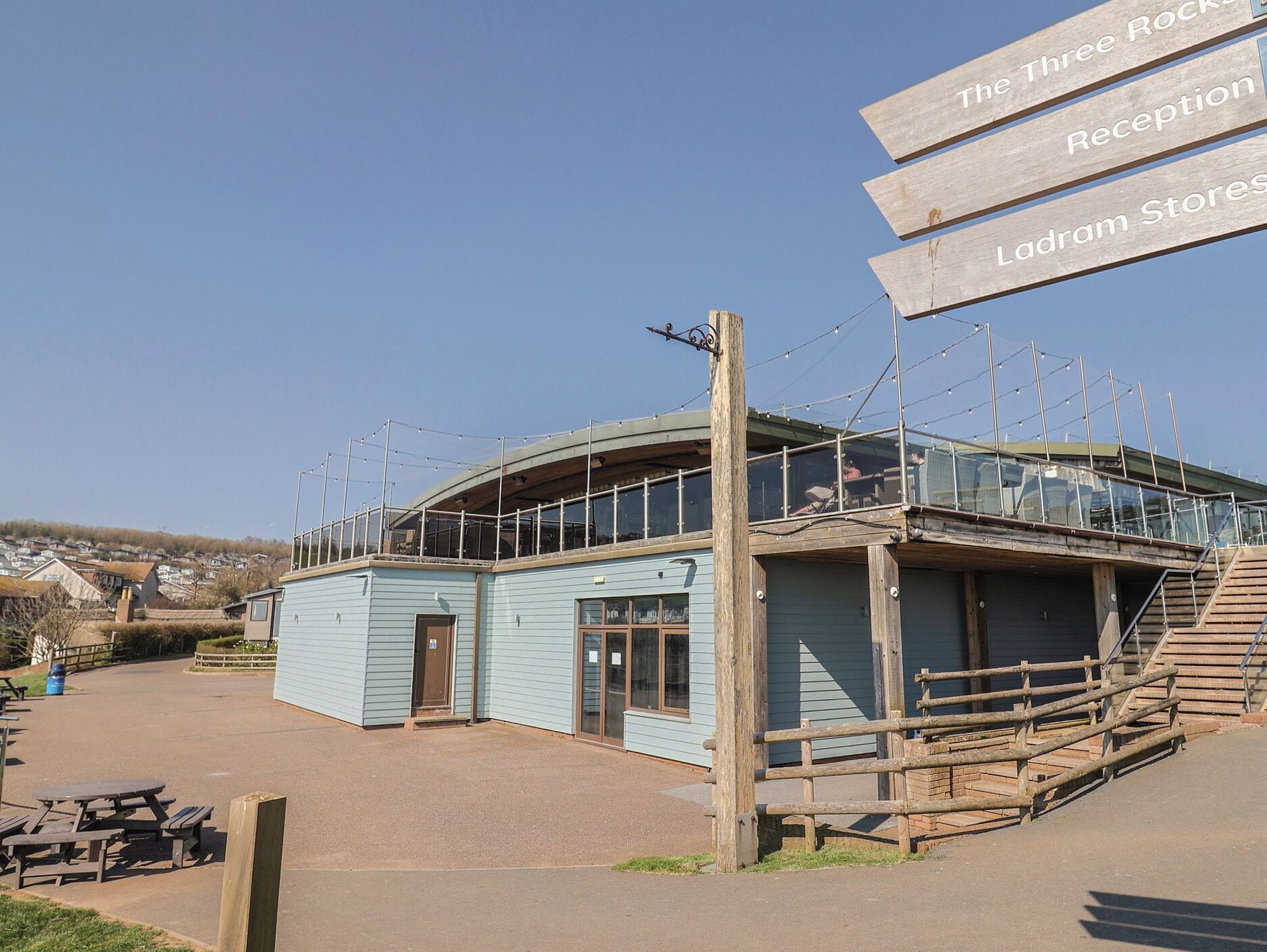 A building with a curved roof, a wooden deck, and a sign indicating 'The Three Rock Reception' and 'Ladram Stores.'