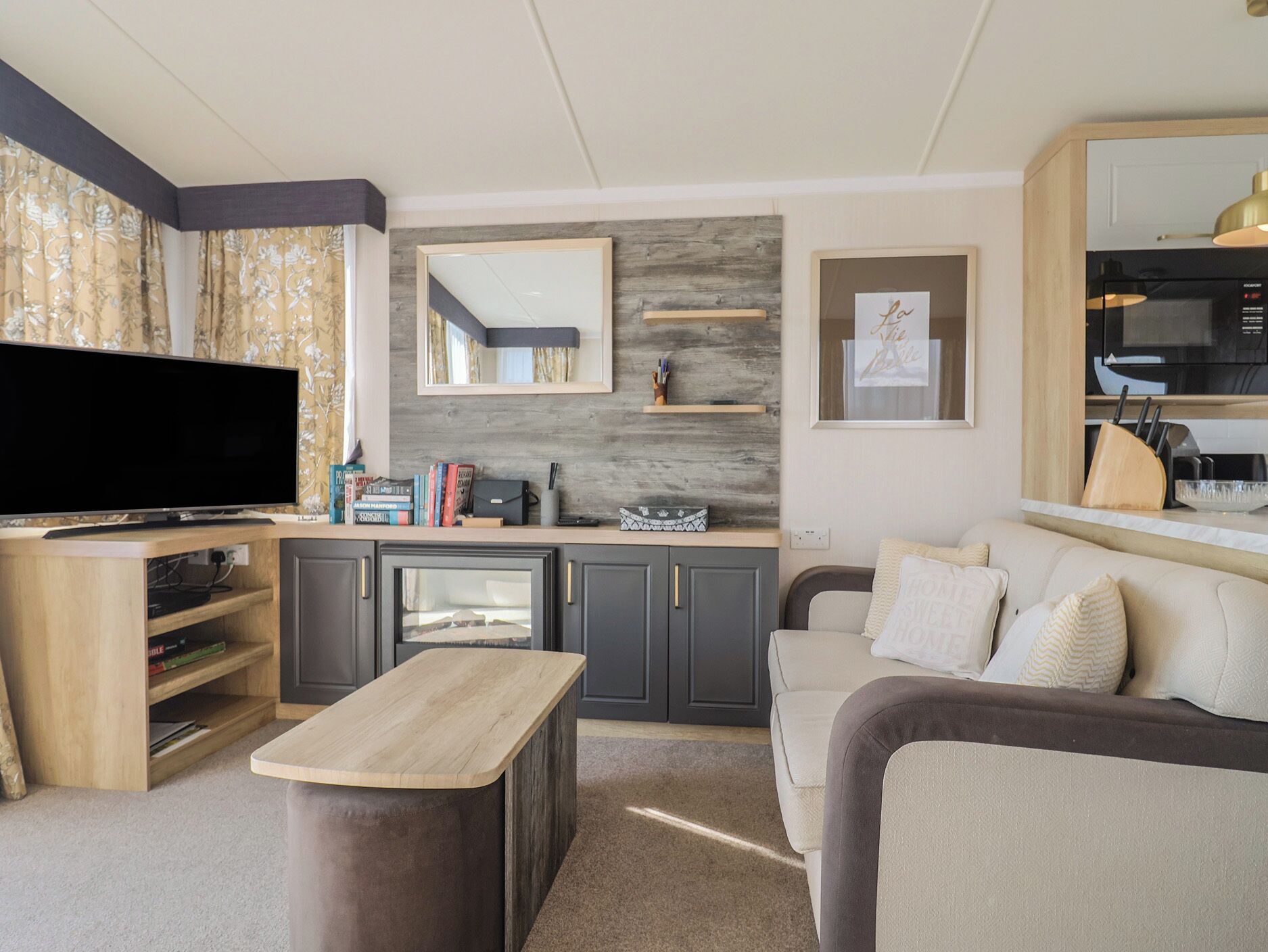 A modern living room with a flat-screen TV, a wooden coffee table, a sofa, a kitchen area with a microwave, and a dining table.