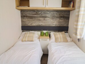 Un dormitorio con dos camas individuales, cabecera de madera, una mesita de noche con lámpara y un estante sobre la cama.