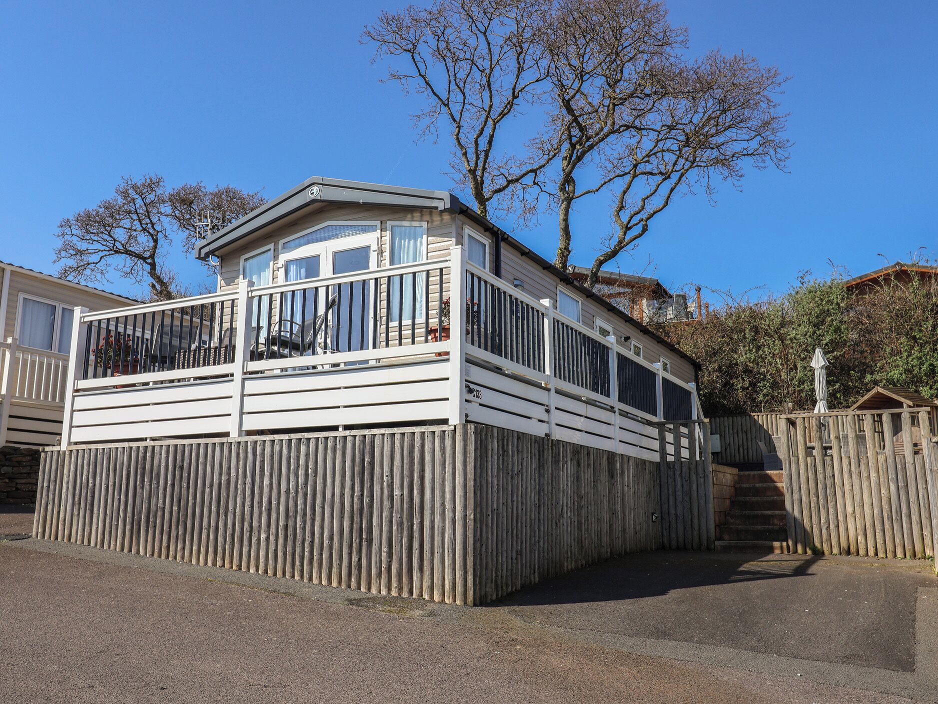 A wooden decked building with a balcony, a fenced area, and a clear sky.