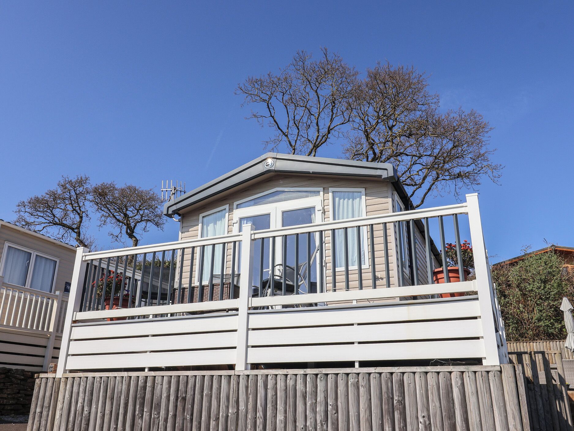 A single-story mobile home with a balcony, a small porch, and a fenced yard.