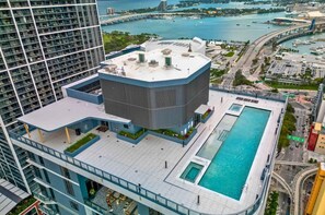 A high-rise building with a rooftop pool, a large glass facade, and a view of a marina and bridge. - F603 - Orange Century Modern 1BR + Den w/ Balcony, Pool & Gym in Downtown Miami (Miami)