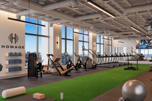A gym with exercise equipment, a wall with 'HOMAGE' branding, large windows, and a view of the city. - F603 - Orange Century Modern 1BR + Den w/ Balcony, Pool & Gym in Downtown Miami (Miami)