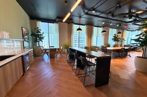 A modern office space with a long communal table, individual workstations, and large windows offering views of the city. - F603 - Orange Century Modern 1BR + Den w/ Balcony, Pool & Gym in Downtown Miami (Miami)