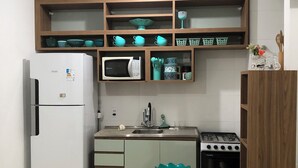 Eine Küche mit Kühlschrank, Mikrowelle, Herd und Holzregalen über der Arbeitsfläche.