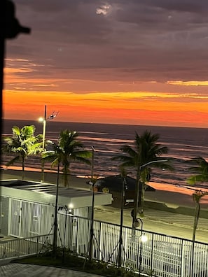A coastal view with a sunset, palm trees, and a building with a sign 'CHICAGO'. - Beachfront apartment with pool for families, pets allowed. (Mongaguá)