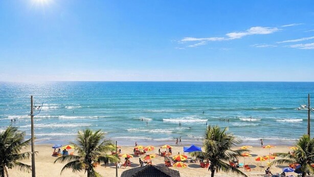 Ein Strand mit Palmen, Sonnenschirmen und Menschen.