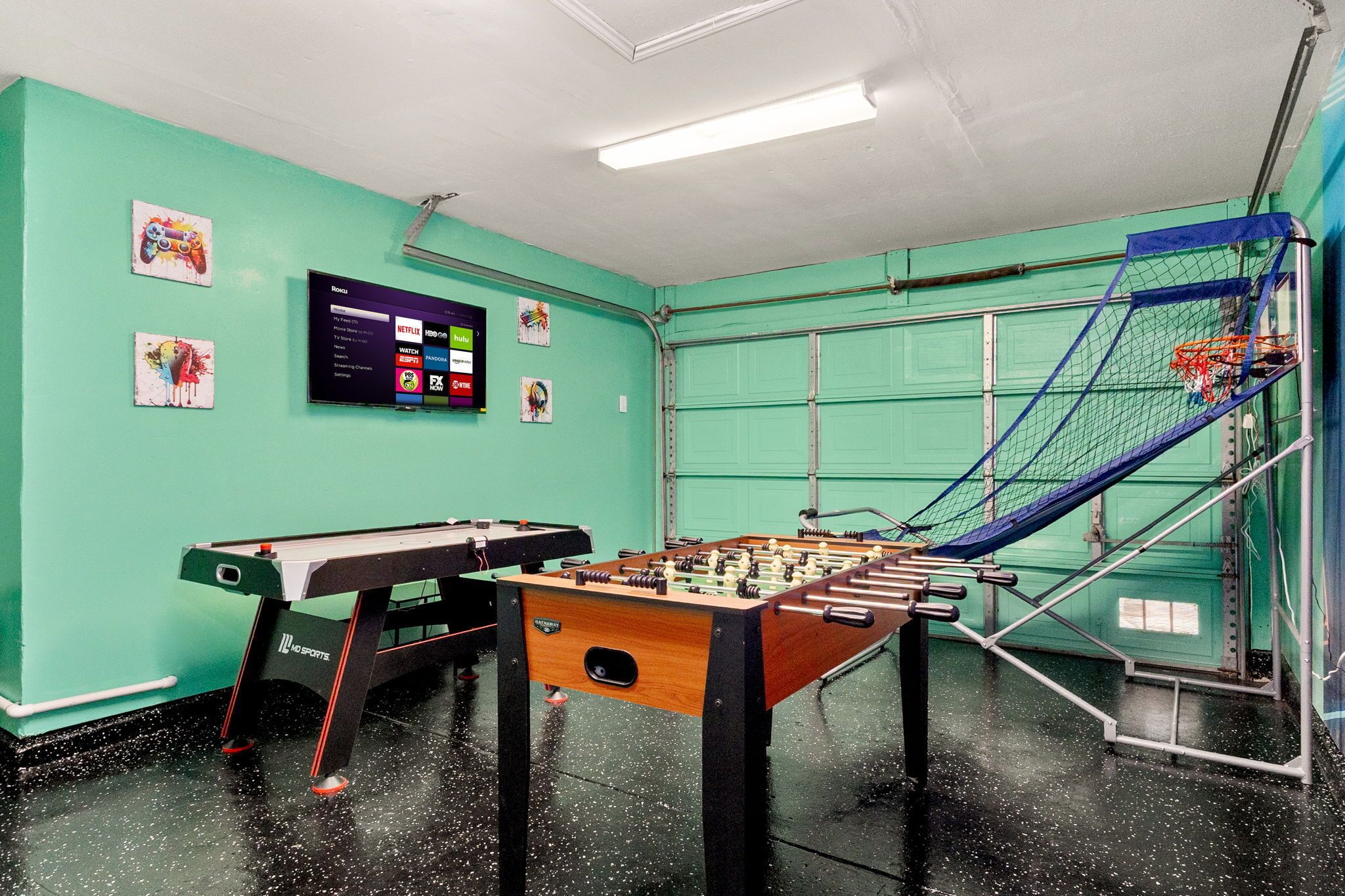 A room with a foosball table, a pool table, and a television displaying a menu.