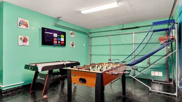 A room with a foosball table, a pool table, and a television displaying a menu.