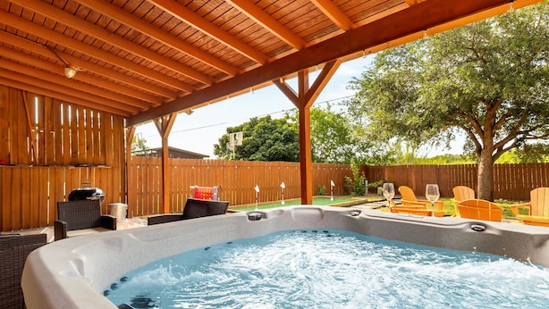 Un bain à remous installé sous une pergola en bois, agrémenté de meubles en osier et de chaises orange.