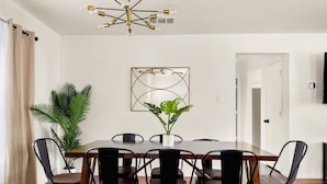 Un coin repas avec une table en bois, des chaises noires, une plante en pot, une œuvre d’art géométrique accrochée au mur et un luminaire au plafond.