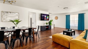 Un salon moderne avec une table à manger en bois, des chaises noires, un canapé jaune et un téléviseur à écran plat fixé au mur.