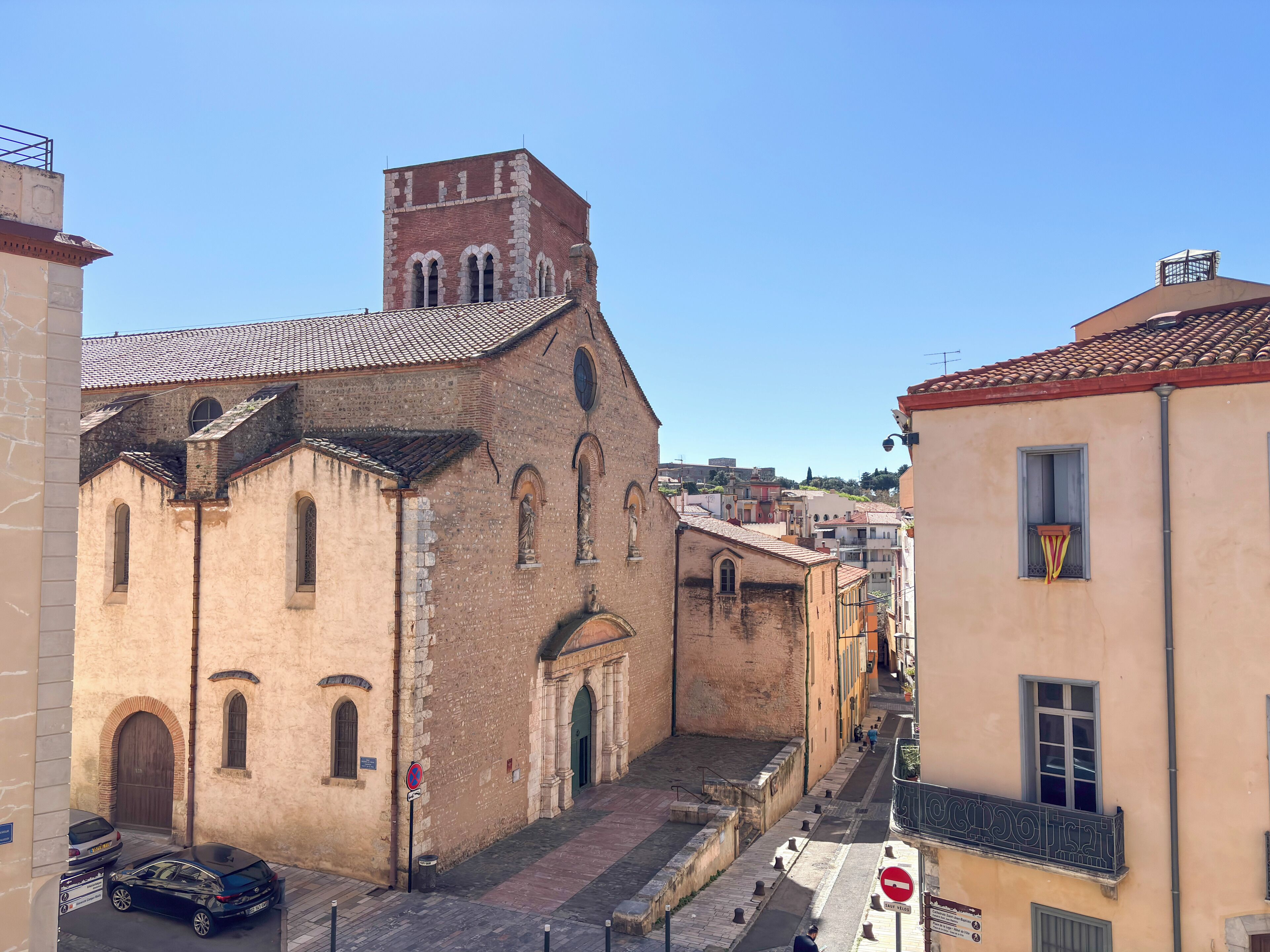 Una calle estrecha con edificios históricos, una iglesia con un campanario y un cielo azul despejado.