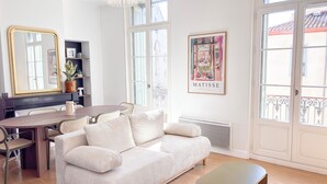 Uma sala de estar moderna com sofá, mesa de jantar, cadeiras, um banco, um candelabro, um espelho grande e uma janela com vista.