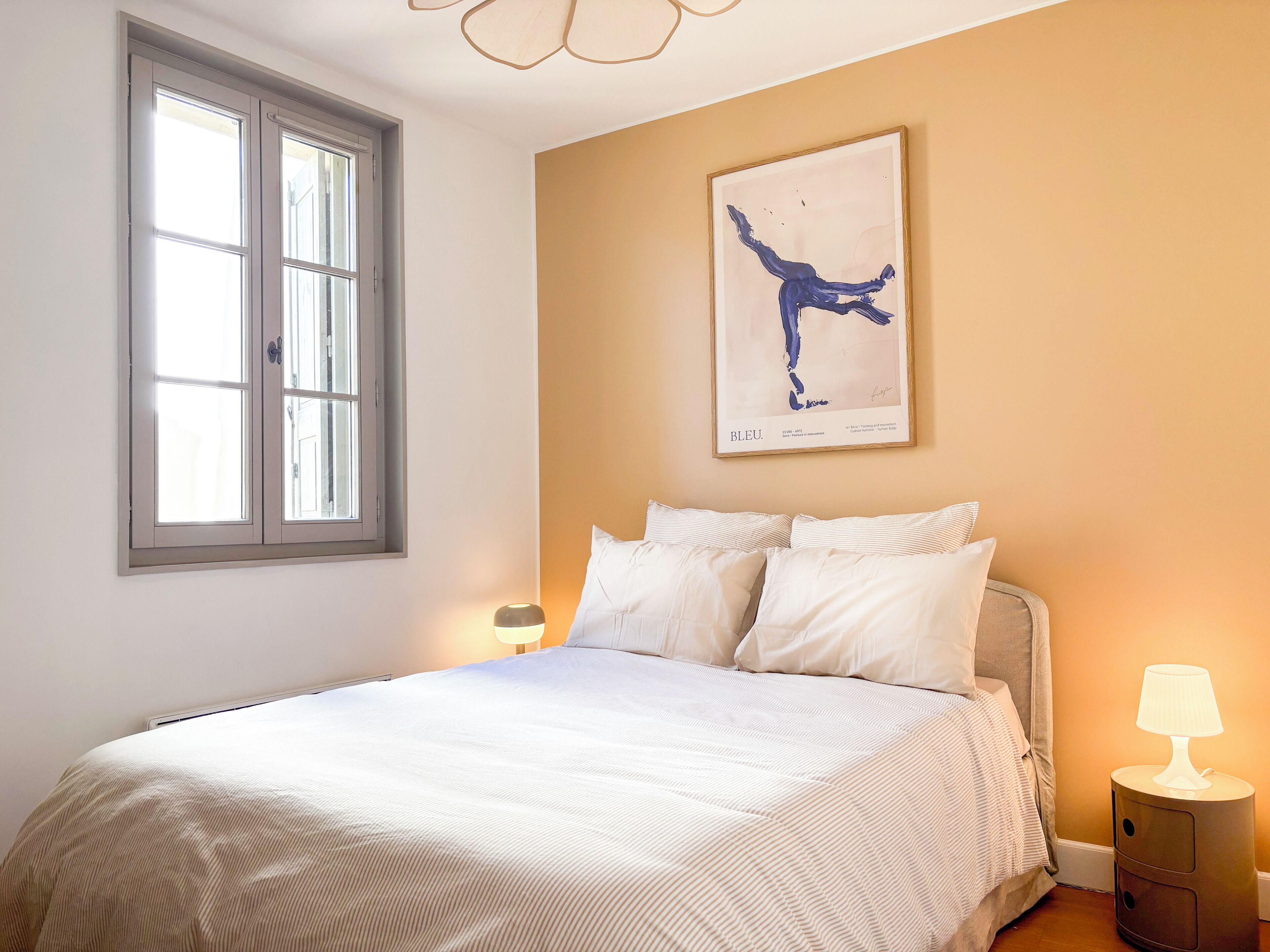 A bedroom with a bed, a window, a wall-mounted artwork, and bedside lamps.