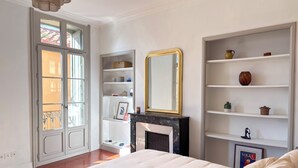 Quarto com cama, lareira, espelho grande e estante com objetos decorativos.